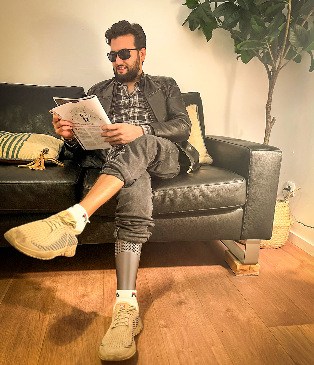 Junger Mann mit Unterschenkelprothese sitzt entspannt auf dem Sofa und liest eine Zeitschrift – Beinprothese im Alltag